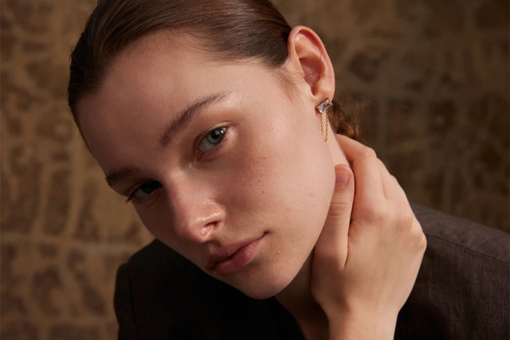 A model showcasing elegant gold earrings with a rectangular crystal and chain design.