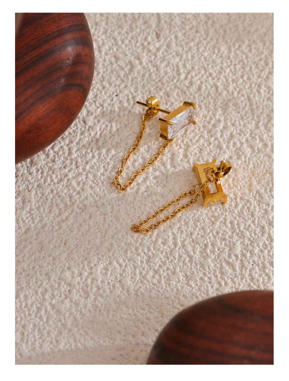 Minimalist and elegant gold earrings with a rectangular crystal and dangling chain.